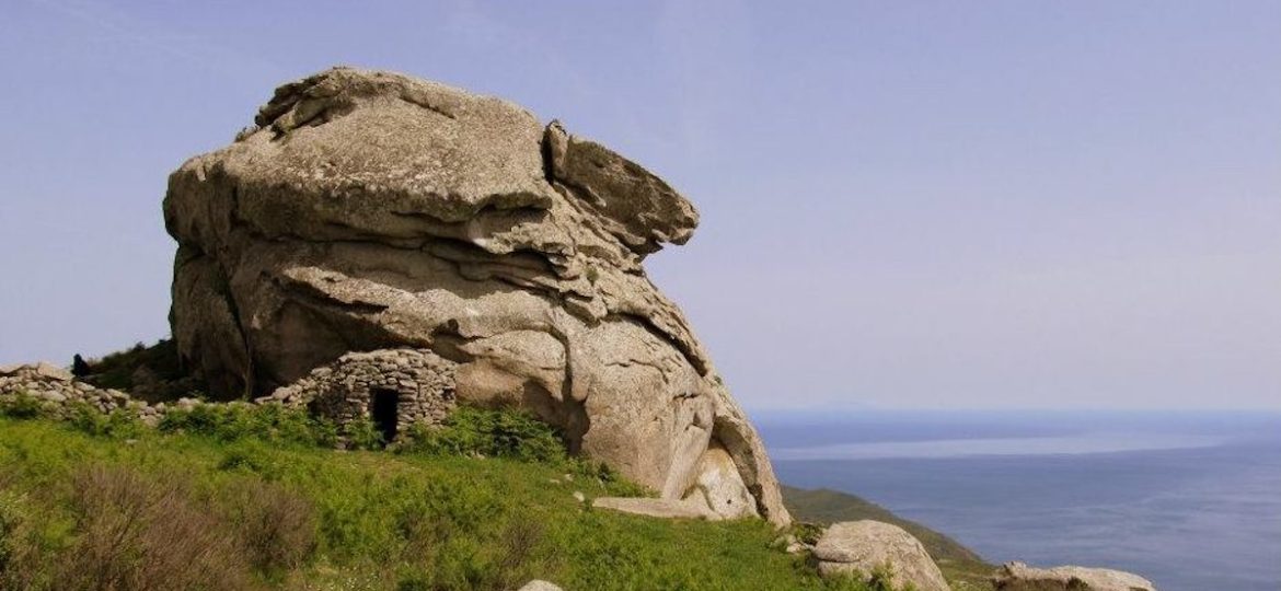 Il Mostro di Pietra sul Monte Capanne, Isola d'Elba, con un antico caprile in pietra alla sua base e vista panoramica sul mare in lontananza.