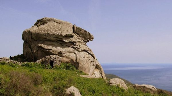 Il Mostro di Pietra sul Monte Capanne, Isola d'Elba, con un antico caprile in pietra alla sua base e vista panoramica sul mare in lontananza.