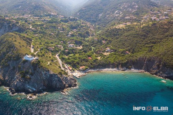 Panoramica dall'alto della costa di Patresi all'Isola d'Elba, che mostra il mare blu intenso, la piccola spiaggia e il faro bianco a picco sulla scogliera.